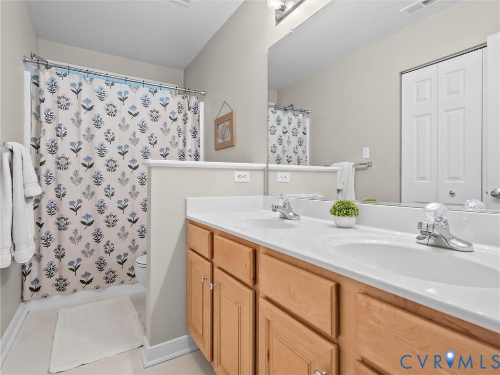 Dual-sink vanity with wood cabinetry, expansive mirror, and overhead lighting