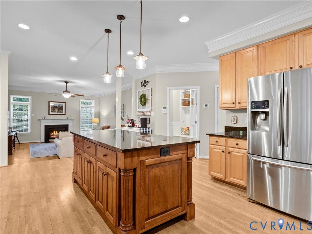 Expansive kitchen island with dark countertop, light wood cabinetry, stainless steel refrigerator, and wood-finish flooring