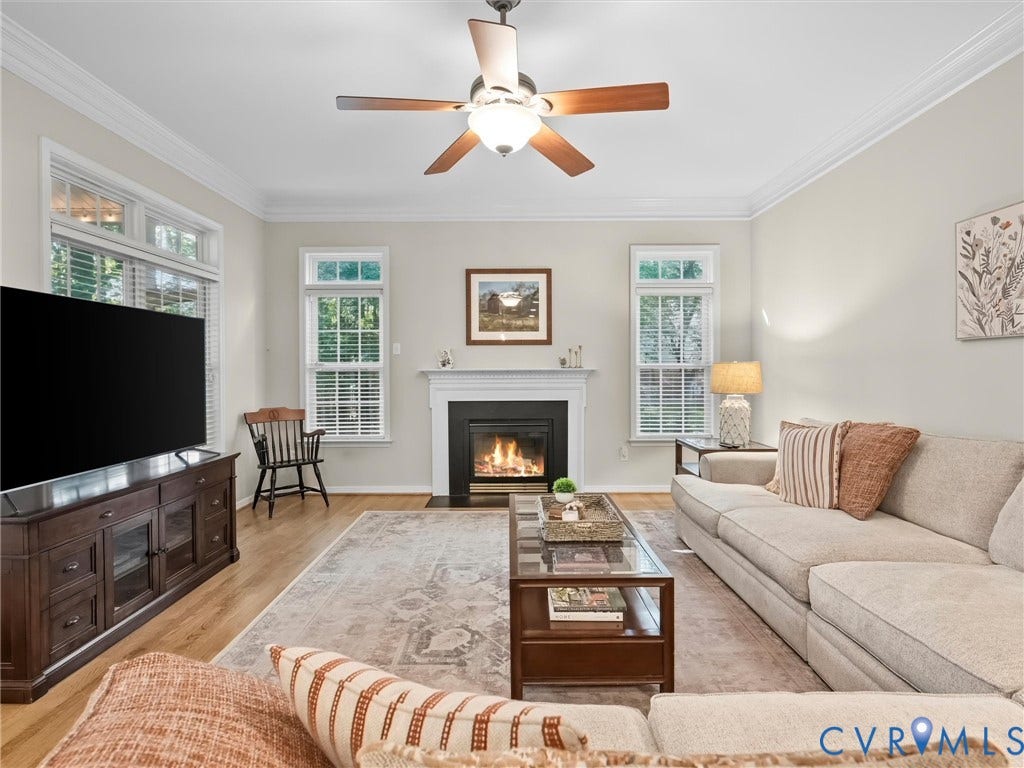 Living area featuring wood-finish flooring, a fireplace with a white mantel, and a ceiling fan