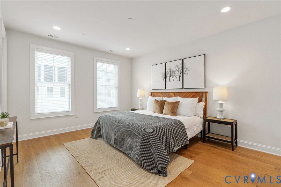 Spacious primary bedroom with hardwood floors, crown molding and multiple windows.