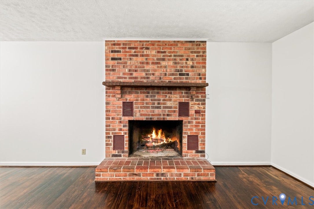 Brick fireplace with hearth, wood mantle, and dark wood-finish flooring