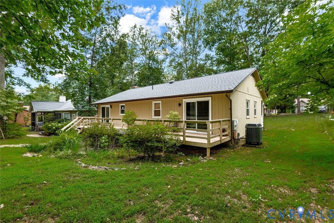 Expansive backyard featuring a large wood deck with railings, sliding glass doors, and mature trees