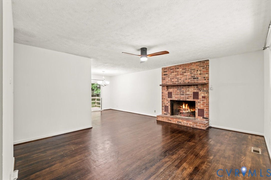 Spacious room featuring wood-finish flooring, a brick fireplace with a mantel, and a ceiling fan