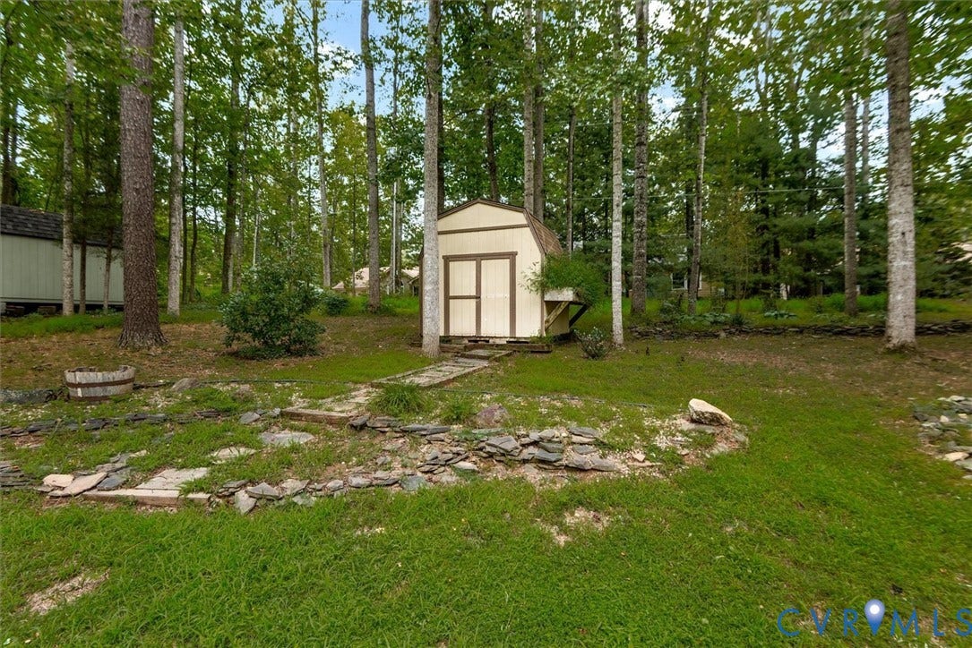 Wooded yard featuring a storage shed, green lawn, and stone-lined landscaping