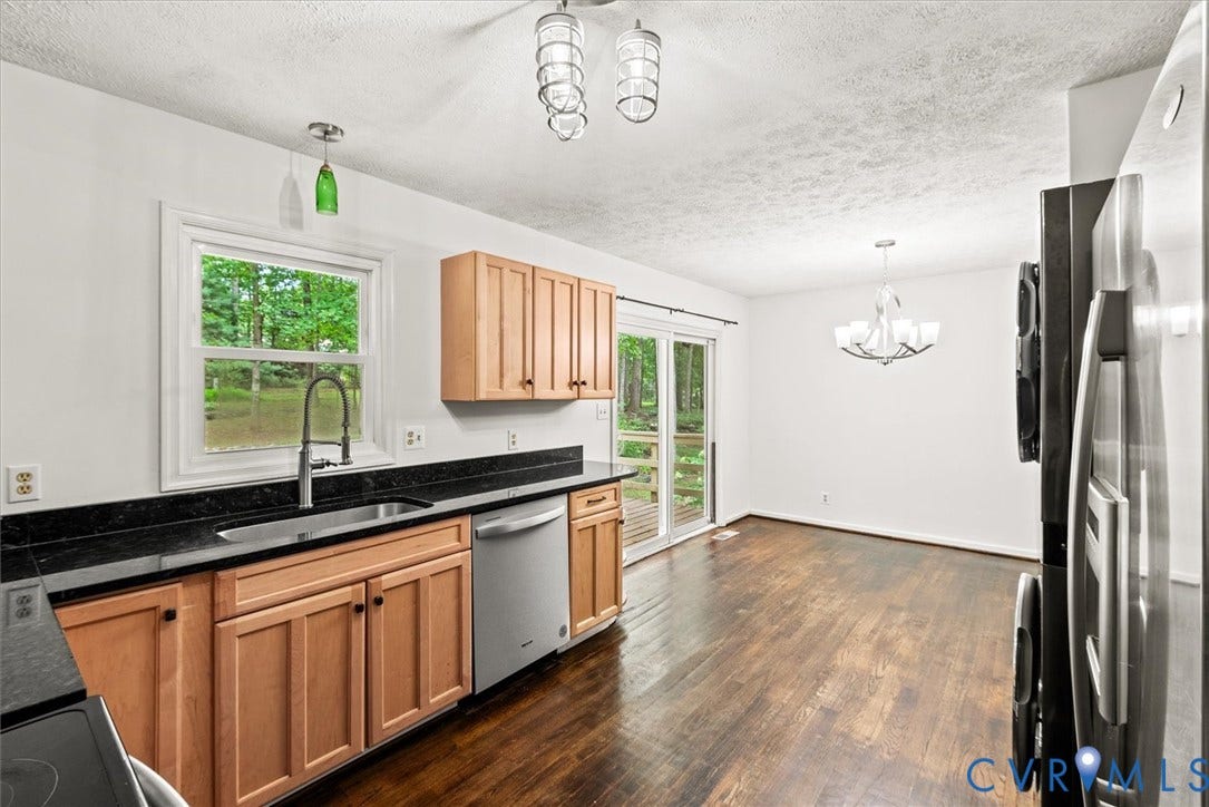 Kitchen featuring wood cabinetry, dark countertops, a stainless steel dishwasher, and dark wood-finish flooring