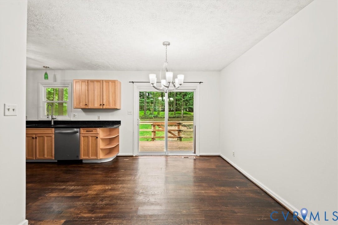 Wood-finish flooring, sliding glass door, overhead lighting fixture, light wood cabinetry, and a black countertop