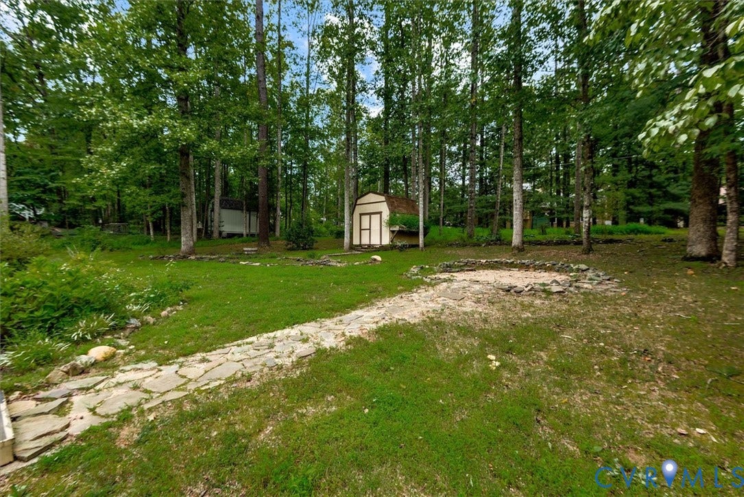 Expansive backyard with a manicured lawn, flagstone pathway, built-in fire pit, and mature trees