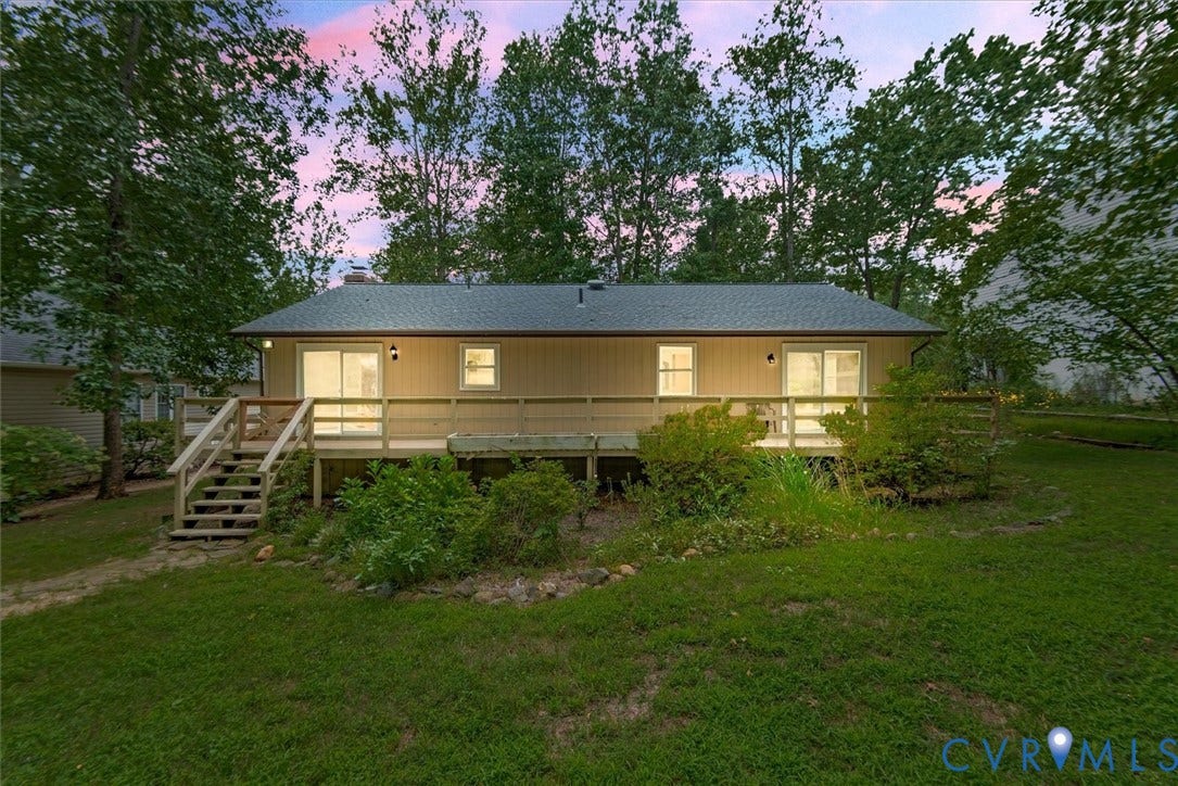 Rear exterior featuring a spacious wooden deck with railings, sliding glass doors, and exterior lighting, surrounded by mature trees