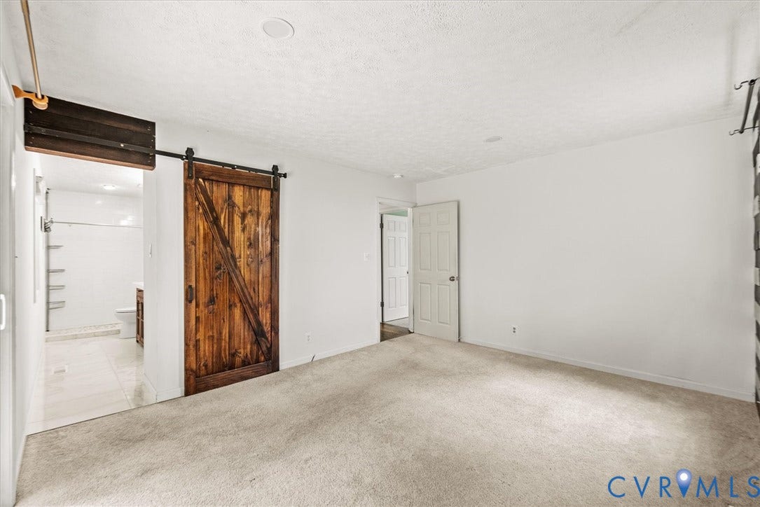 Carpeted flooring, white painted walls, wood-finish barn door, white paneled door, and recessed lighting