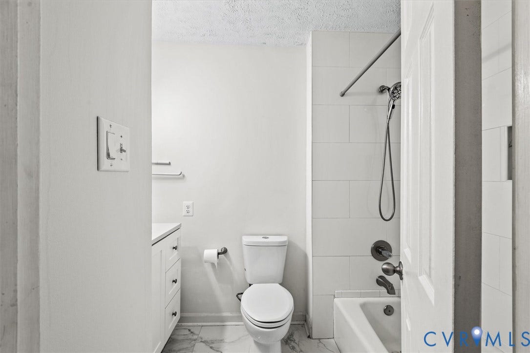 White bathroom with a built-in tub and shower, subway tile surround, white vanity, and light-toned flooring