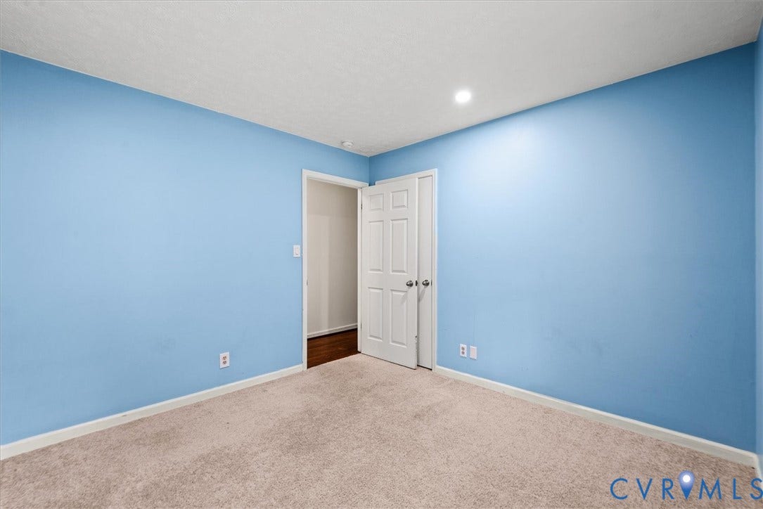Neutral-toned carpeting, light blue painted walls, white trim, and a white interior door with a silver-toned doorknob
