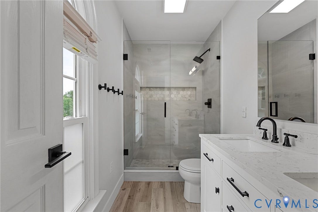11100 Glen Hollow Court, Henrico, VA 23233 Glass-enclosed shower with a recessed shelf, single vanity with an integrated sink, wood-finish flooring, and black hardware accents