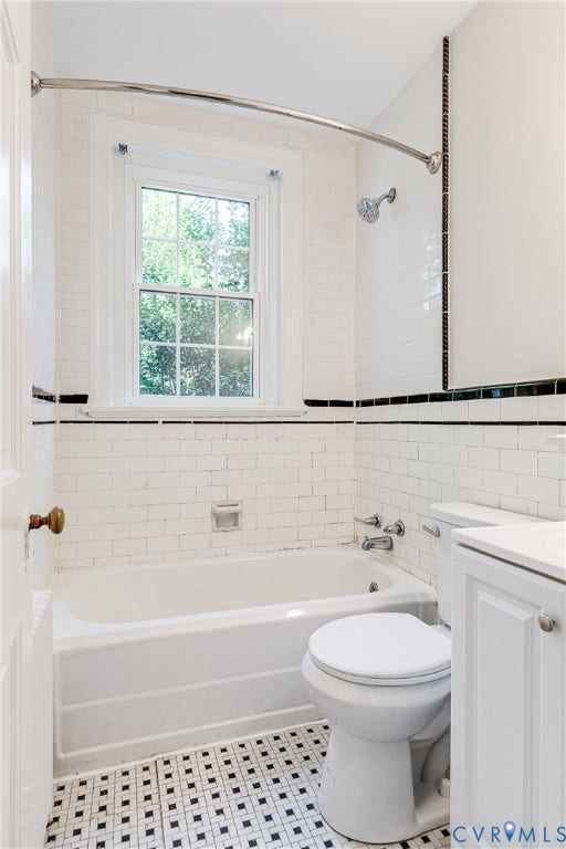 4010 Patterson Avenue, #1stfl, Richmond, VA 23221 White subway tile walls with black accent trim, a window with natural light, a white bathtub, a toilet, and a vanity with white cabinetry