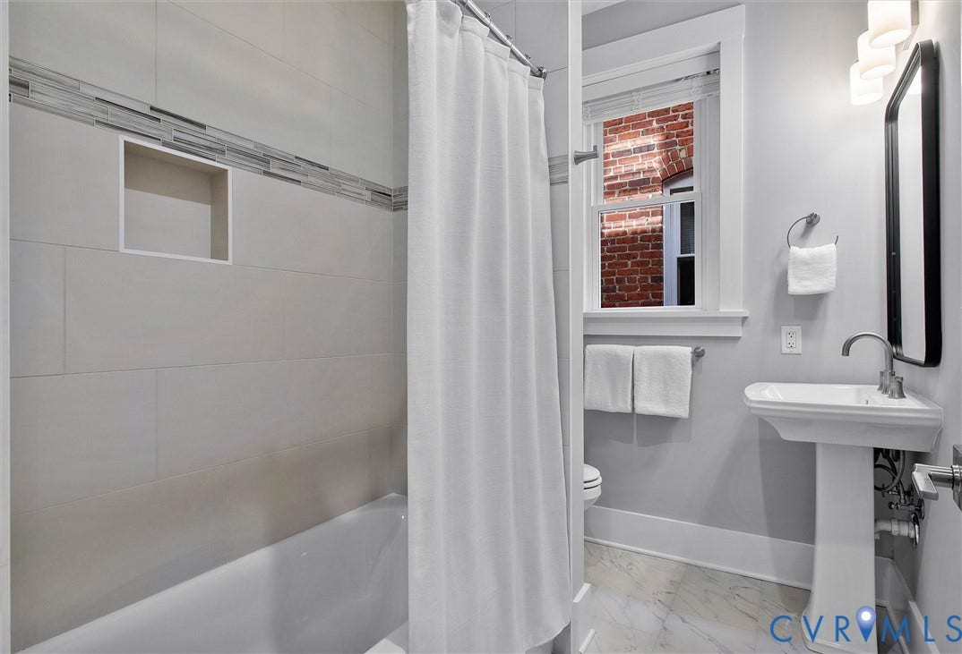 2902 Idlewood, #5, Richmond, VA 23221 Bathroom with a pedestal sink, a rectangular mirror, a window, and a bathtub with a tiled surround featuring an accent band and a recessed niche