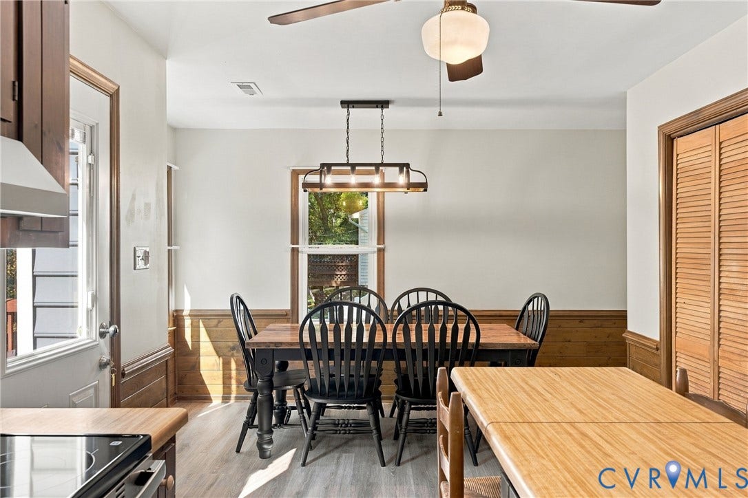 Dining area featuring wood-plank wainscoting, linear multi-bulb pendant lighting, wood-finish flooring, a ceiling fan, and bi-fold louvered closet doors