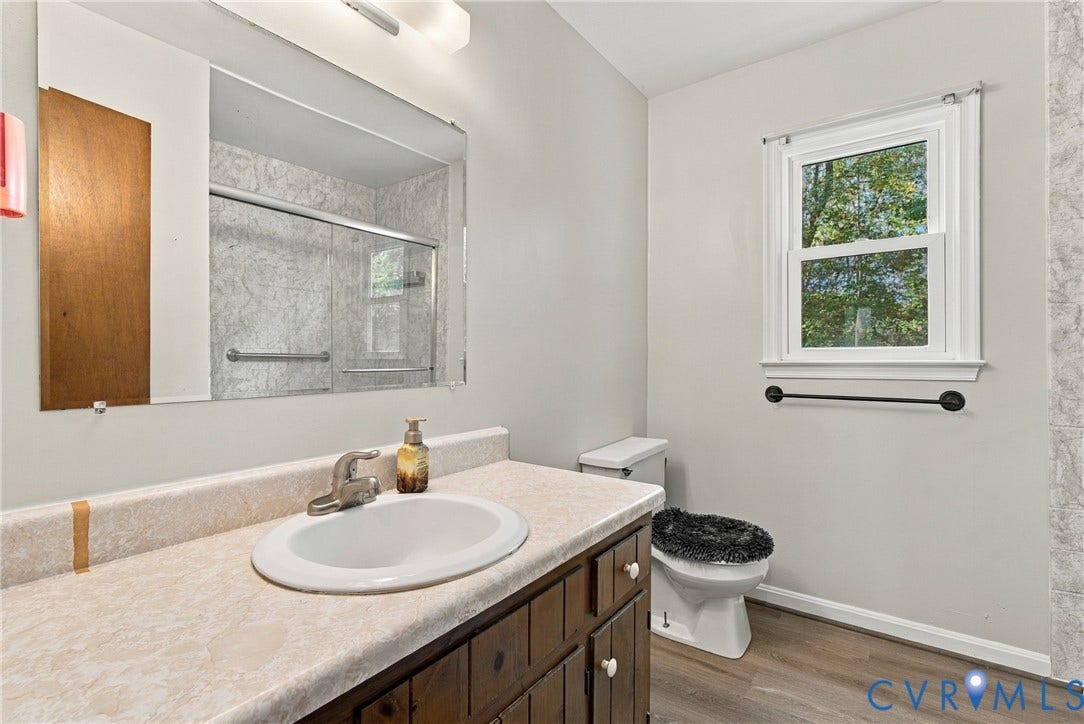 Bathroom featuring a wood-tone vanity, laminate countertop with integrated sink, large wall-mounted mirror, single-hung window, and wood-finish flooring