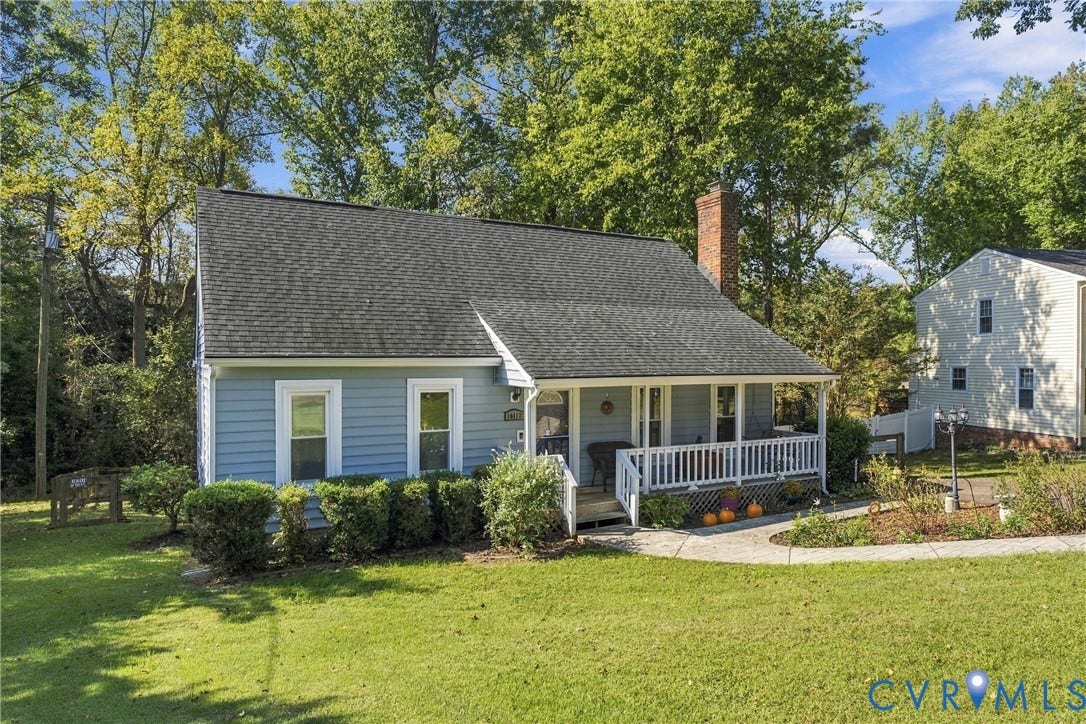 Blue siding exterior featuring a covered front porch with white railing, a masonry chimney, and a stone-paver walkway