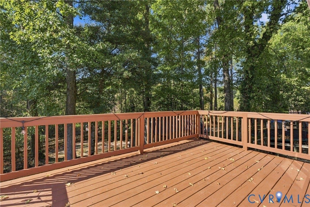 Raised wooden deck featuring horizontal plank flooring and a perimeter balustrade railing, surrounded by mature trees