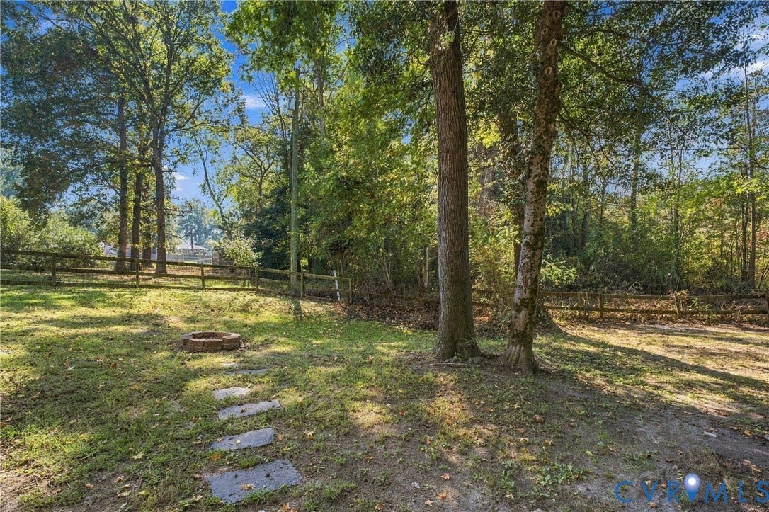 Spacious outdoor area featuring mature trees, a natural stone fire pit, a stone paver path, and perimeter wooden fencing