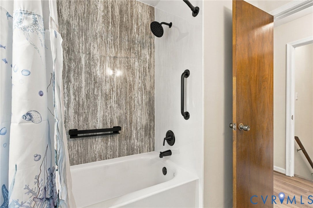 Bathtub enclosure with matte black fixtures, textured stone-finish surround, and integrated wall-mounted grab bars