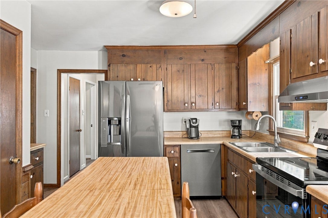 Kitchen featuring natural wood cabinetry, stainless steel side-by-side refrigerator, stainless steel dishwasher, integrated island with wood countertop, and stainless steel range hood