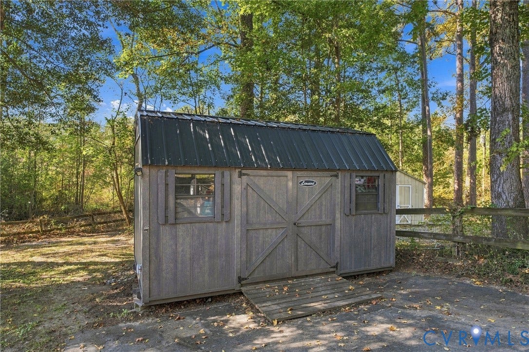 Detached storage building featuring a dark metal gambrel roof, gray vertical wood-textured siding, double-door entry with ramp, and two side windows