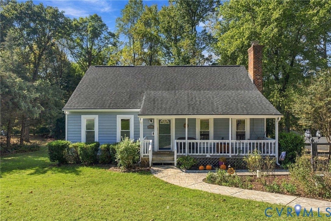Single-story residence featuring light blue horizontal siding, a covered front porch with a white balustrade, a stone-patterned walkway, and an exterior brick chimney