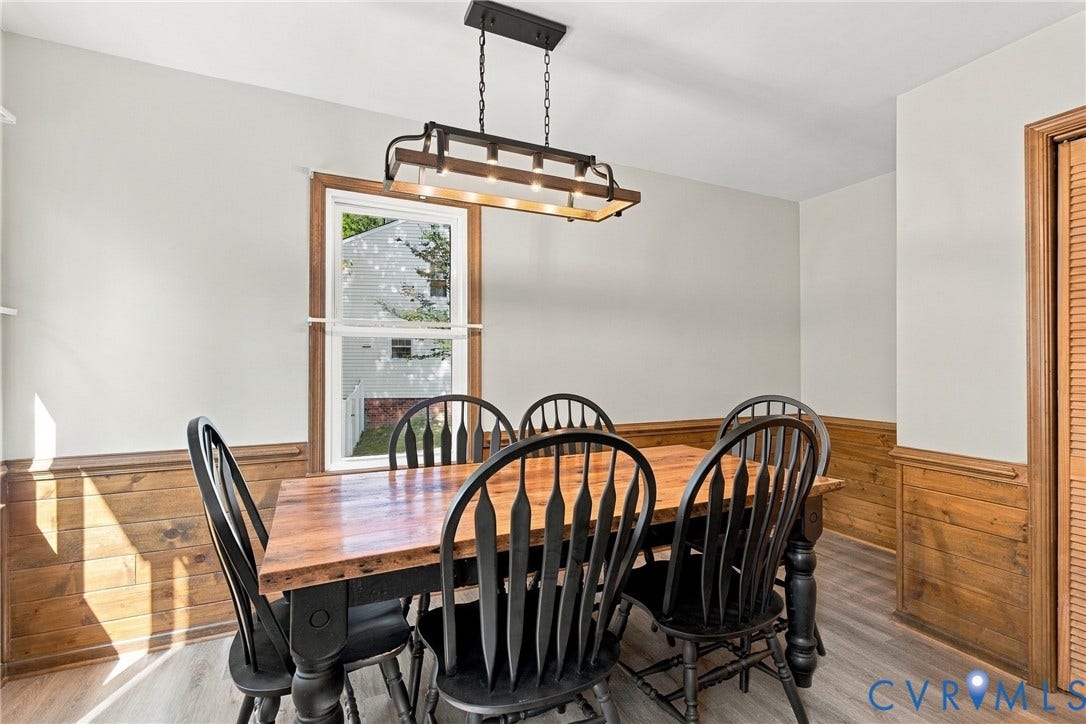 Dining area featuring wood-paneled wainscoting, wood-finish flooring, and a rectangular metal chandelier with exposed bulbs