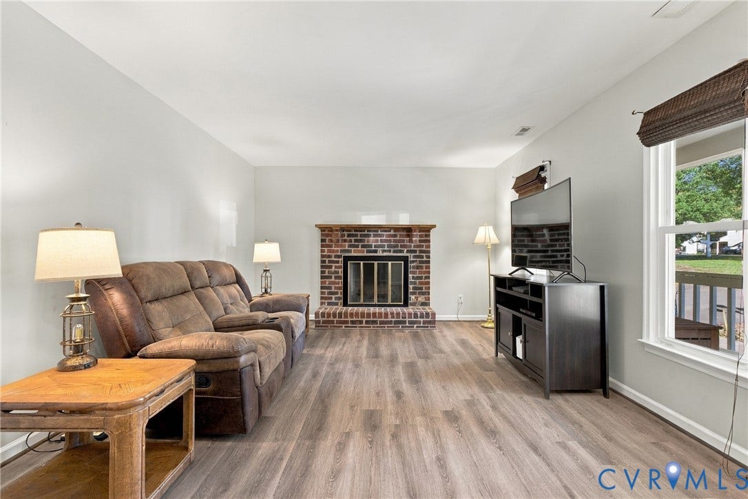 Living area featuring wood-finish flooring, a floor-to-ceiling brick fireplace with a wood mantel, and large windows