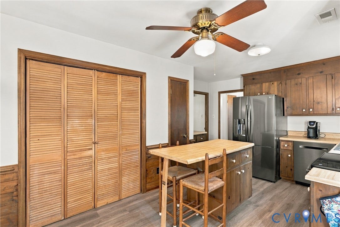 Kitchen featuring wood-toned cabinetry, wood-finish flooring, louvered bi-fold closet doors, stainless steel refrigerator, and ceiling fan with integrated lighting