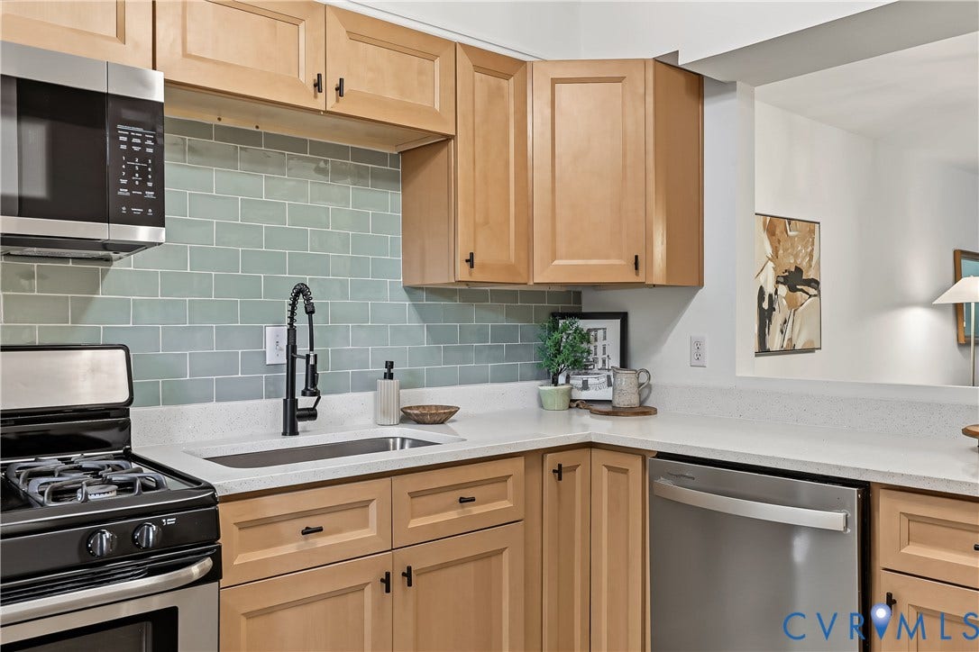 10272 Iron Mill Road, North Chesterfield, VA 23235 Kitchen featuring light wood-finish cabinetry, light-toned countertops, a light blue subway tile backsplash, a stainless steel dishwasher, and a black pull-down faucet
