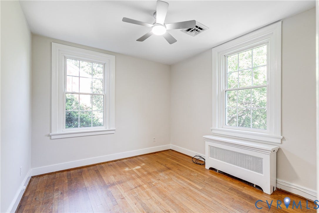4010 Patterson Avenue, #2ndfl, Richmond, VA 23221 Hardwood flooring, two large windows with white trim, a ceiling fan, and a radiator with a decorative cover