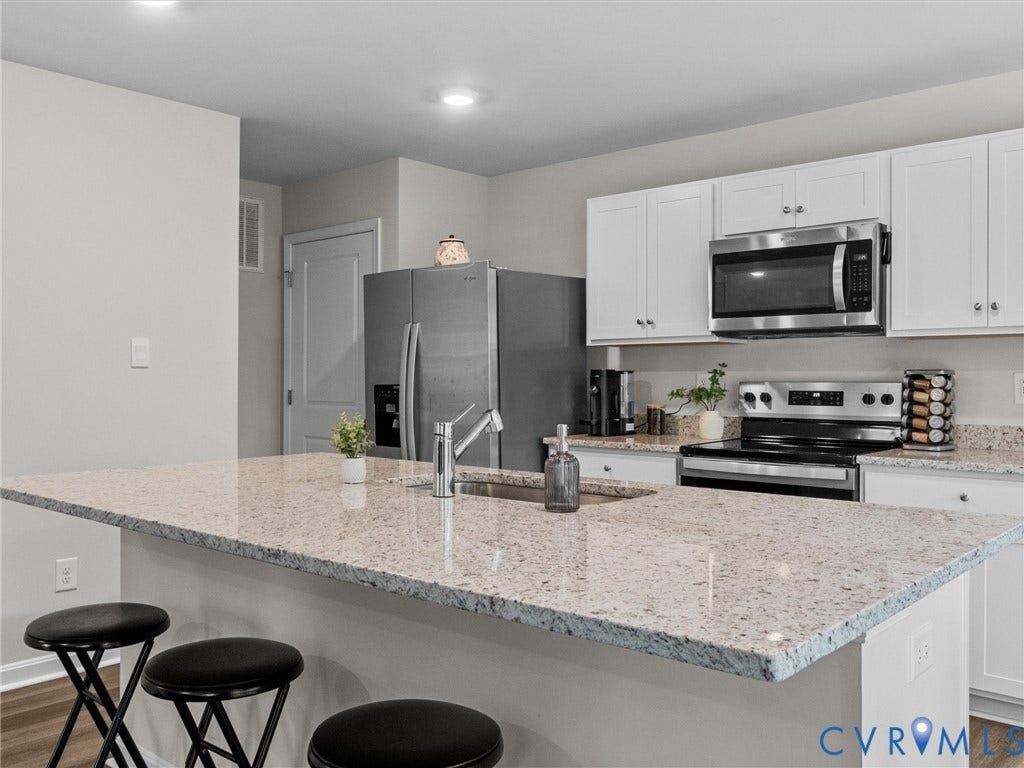 6901 Switch Cane Court, The Arbors, New Kent, VA 23141 Kitchen featuring a central island with a sink, light-toned countertops, white cabinetry, stainless steel appliances, and wood-finish flooring