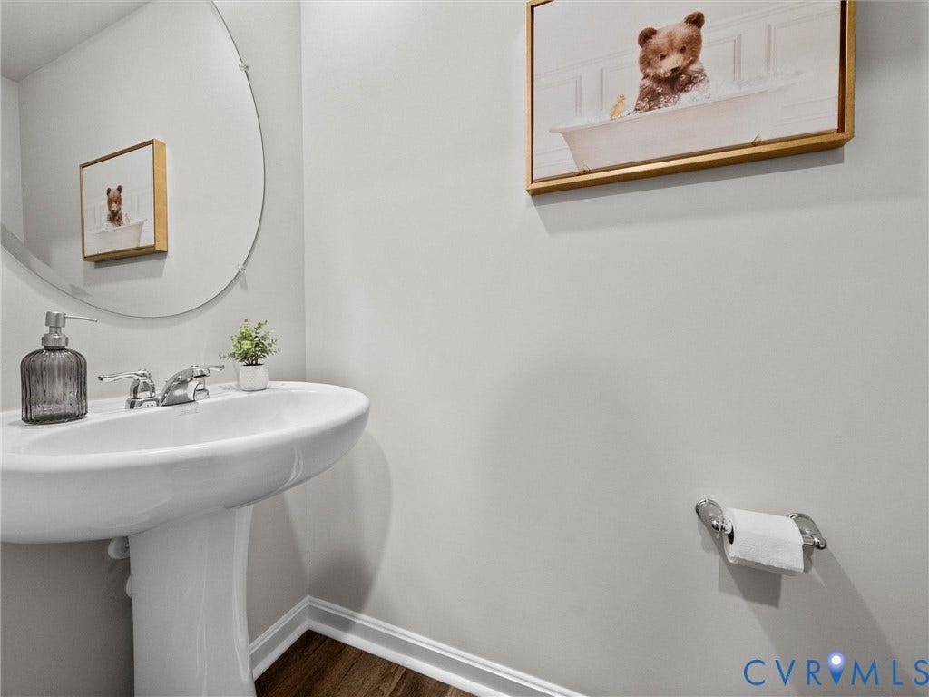 6901 Switch Cane Court, The Arbors, New Kent, VA 23141 Pedestal sink with chrome faucet, circular mirror, and wood-finish flooring