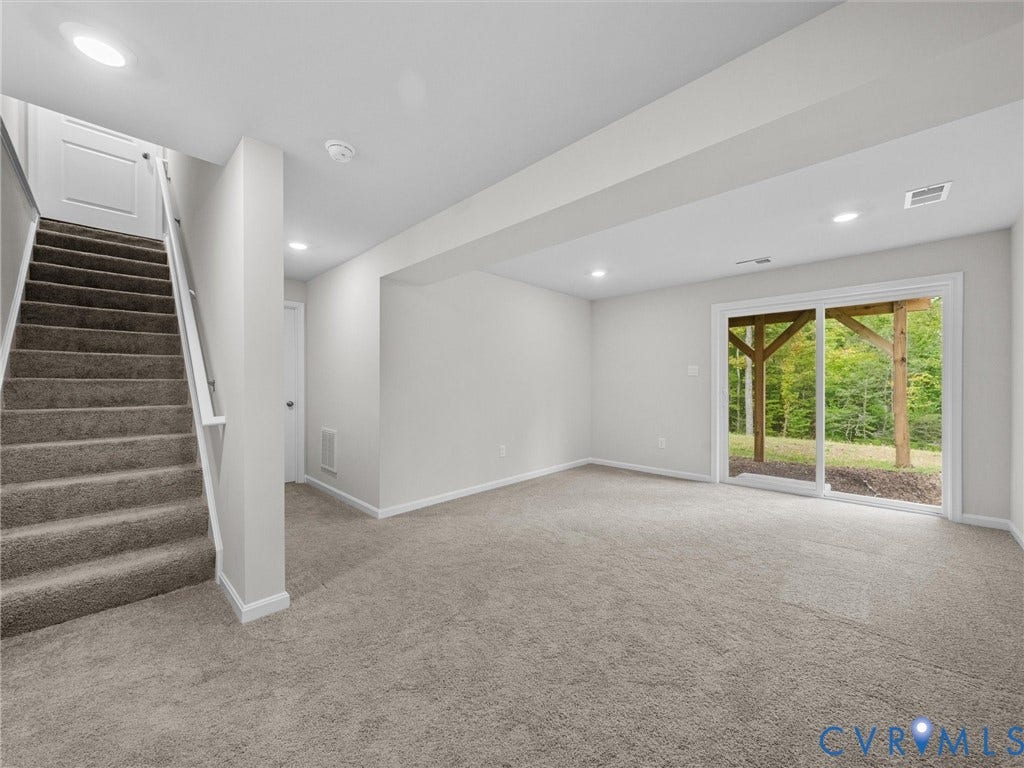 6901 Switch Cane Court, The Arbors, New Kent, VA 23141 Spacious room with plush gray carpeting, recessed ceiling lighting, a sliding glass door providing natural light, and a carpeted staircase with white railings