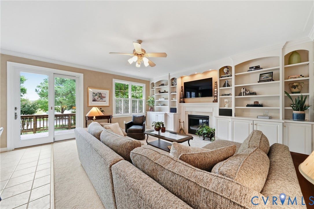 Built-in shelving and cabinetry, fireplace, sliding glass door, multiple windows with plantation shutters, ceiling fan
