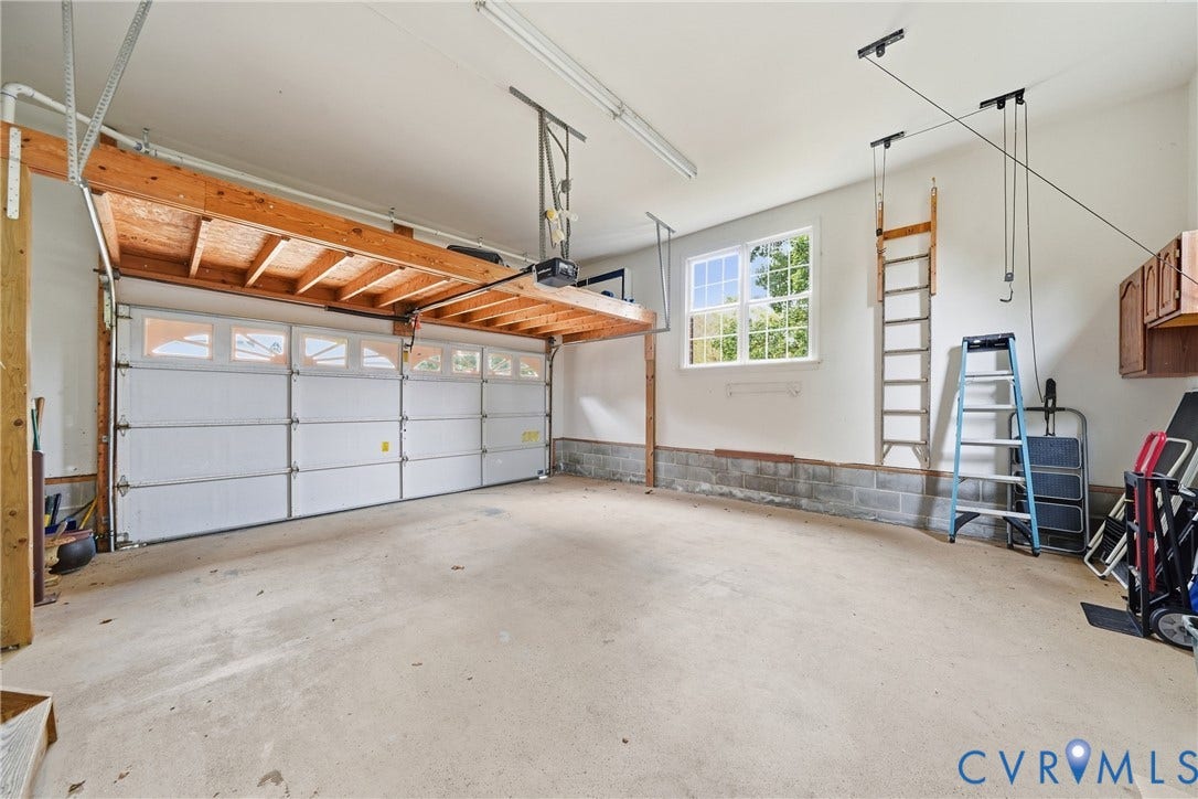 Attached garage with an overhead door featuring transom windows, concrete flooring, and a built-in storage shelf