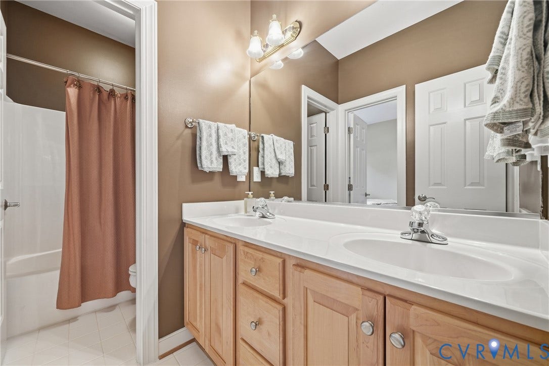Dual vanity with wood-finish cabinetry, white countertops, and chrome fixtures