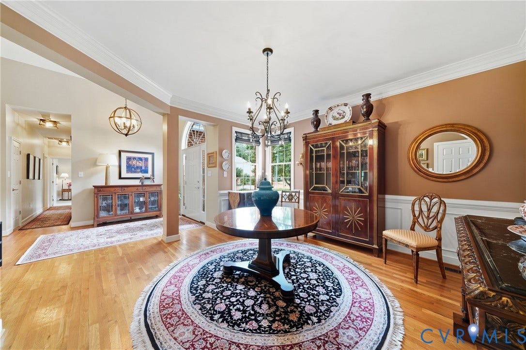 Hardwood flooring, arched entryway with transom window, wainscoting, crown molding, and chandelier lighting