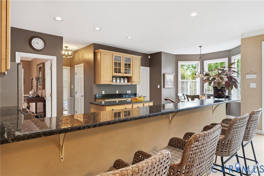 Kitchen featuring granite countertops, wood cabinetry, recessed lighting, and a bay window with plantation shutters