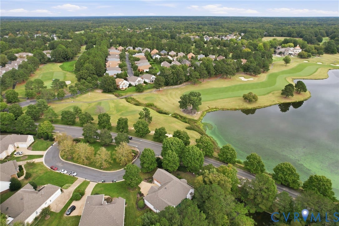 Aerial perspective showcasing a residential community with abundant mature trees, multiple golf course greens, and a substantial body of water