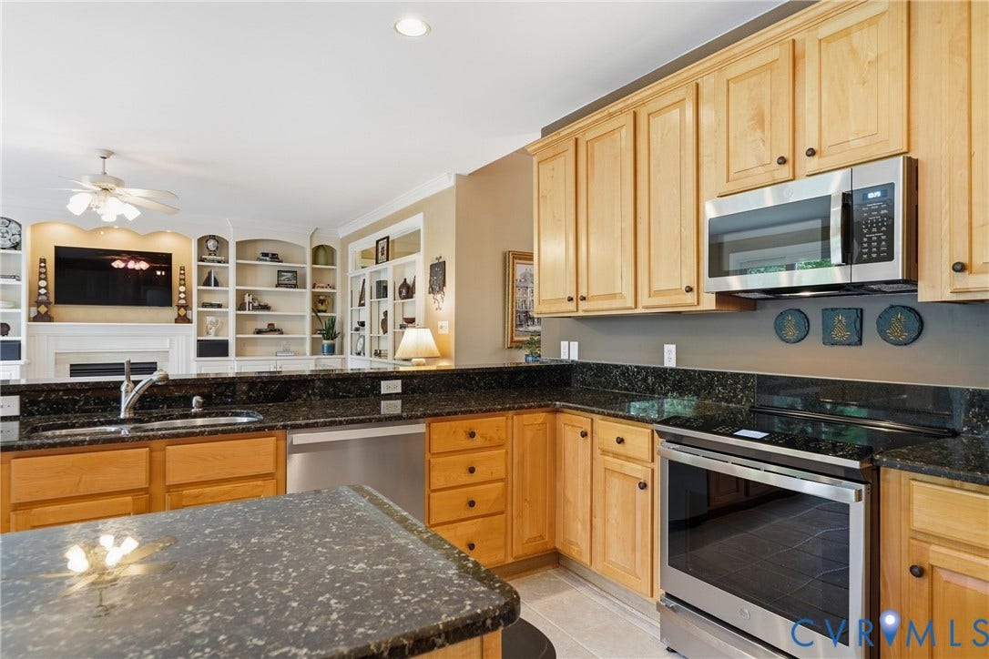 Kitchen featuring light wood cabinetry, dark speckled countertops, stainless steel appliances, and a built-in sink