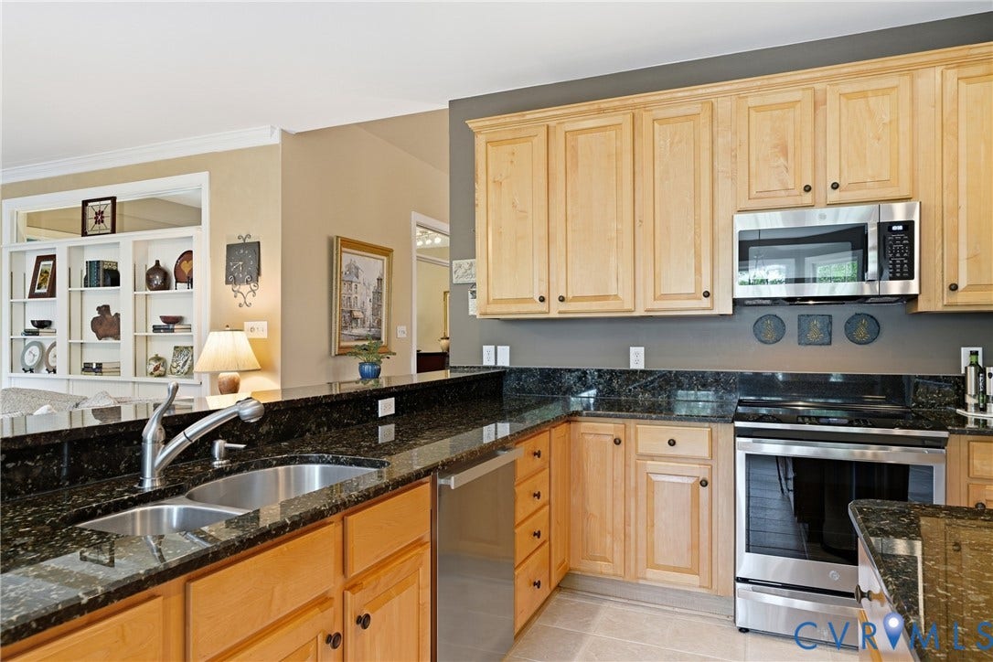 Kitchen featuring light wood cabinetry, dark speckled countertops, stainless steel appliances, and a built-in double basin sink