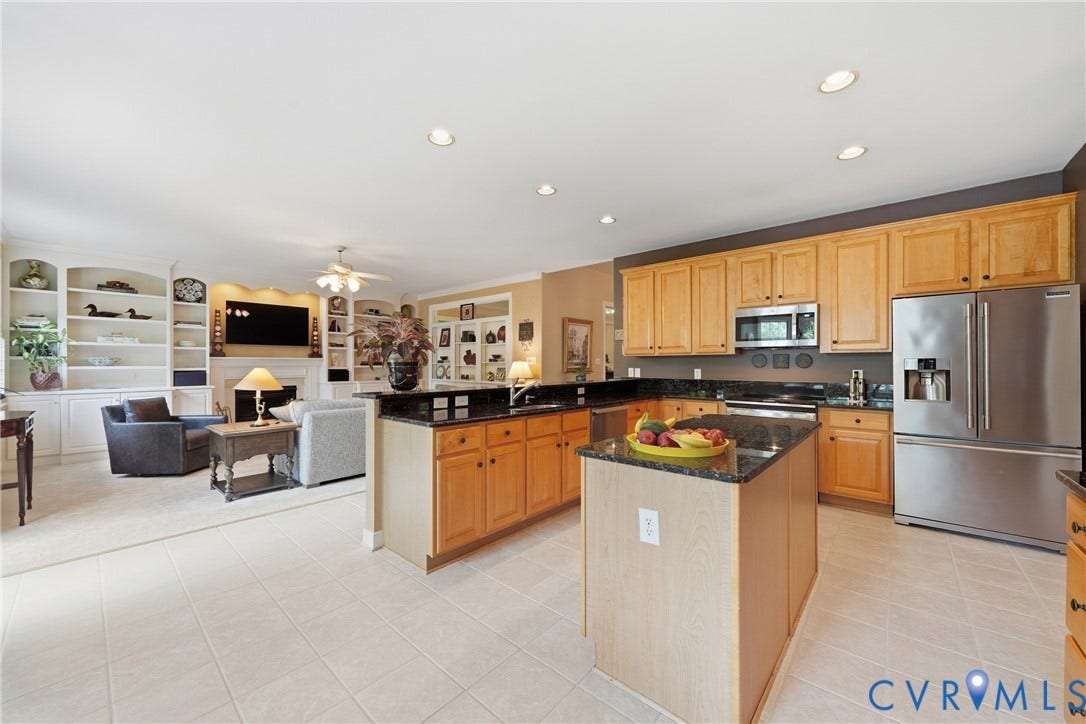 Kitchen featuring light wood cabinetry, a central island, stainless steel appliances, and dark granite countertops