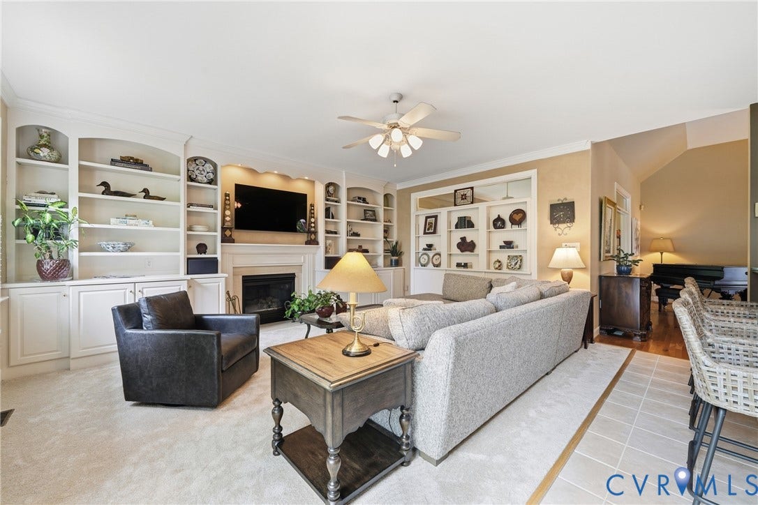 Built-in shelving, fireplace, ceiling fan, carpet flooring, and tile flooring