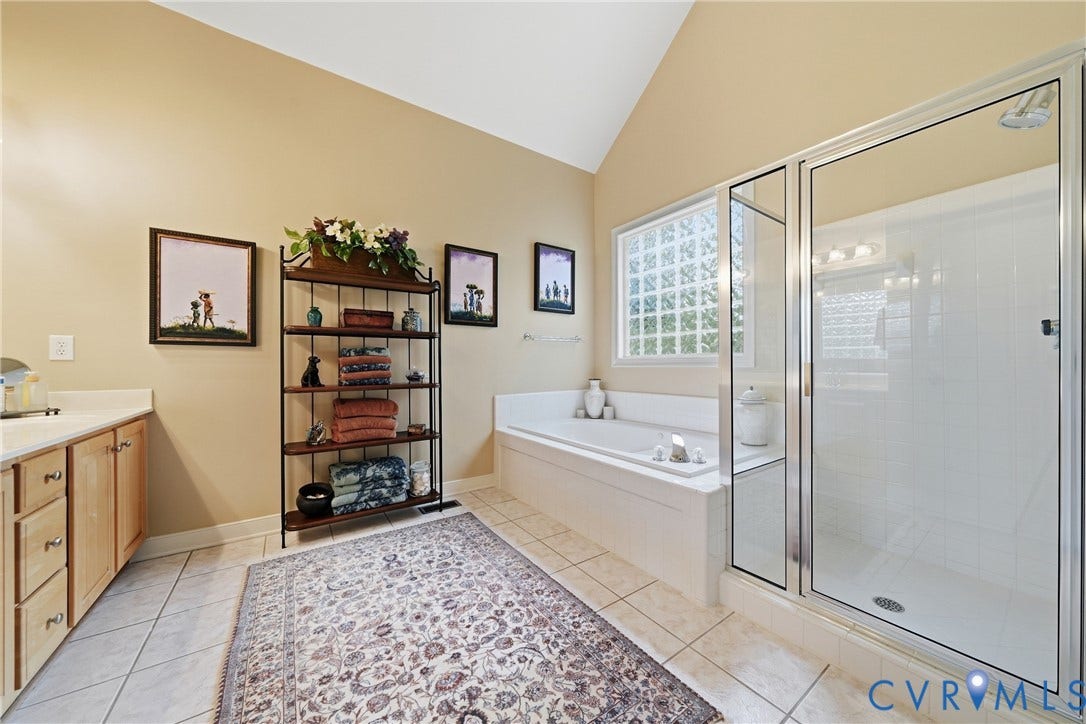 Vaulted ceiling with a transom window, a deep soaking tub, a separate glass-enclosed shower, and a light wood-finish vanity with countertop