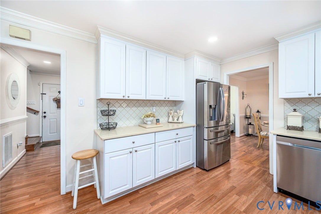 Kitchen featuring wood-finish flooring, white cabinetry, integrated stainless steel refrigerator, and light countertops with a patterned tile backsplash