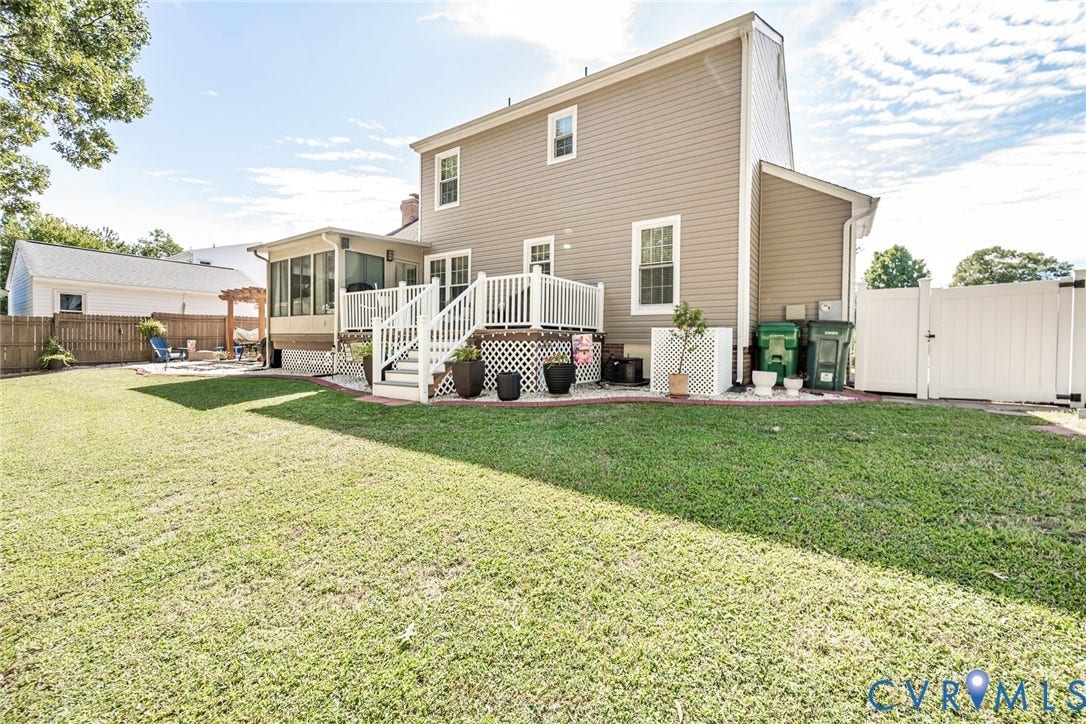 Expansive grassy yard featuring a multi-level deck with white railings, an enclosed sunroom, and a pergola-covered patio