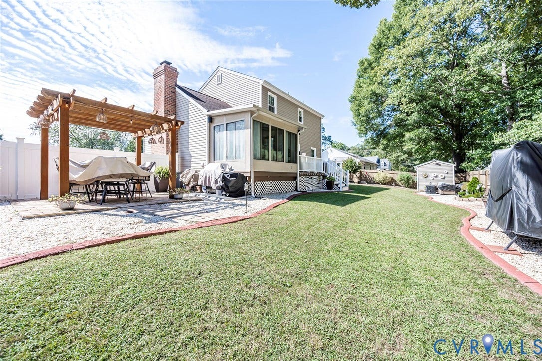 Expansive backyard featuring a pergola, gravel patio, privacy fencing, sunroom extension, and a detached storage shed