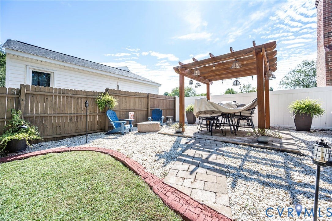 Wood pergola with integrated string lighting, stone paver patio, gravel hardscaping, and a wood privacy fence